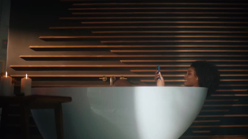 A woman is texting on her phone while in a bathtub