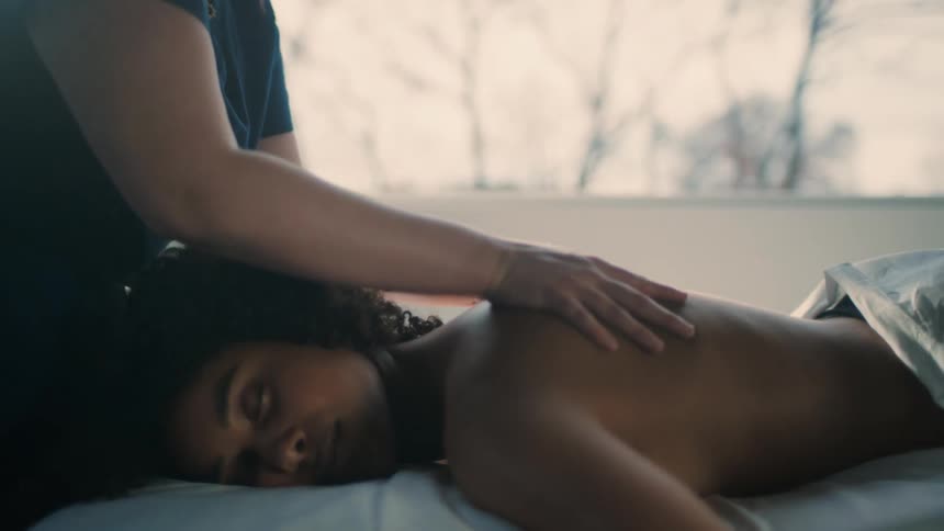Masseuse massages back of woman lying on her front with her eyes closed