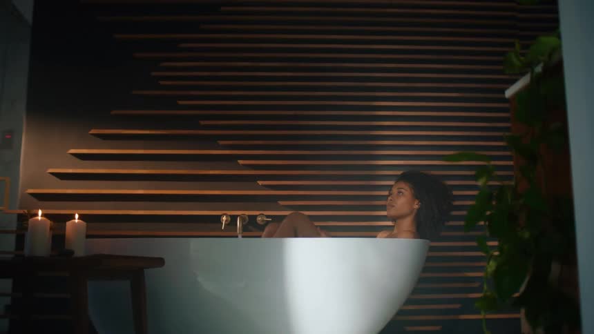 Woman bathes in bathtub in bathroom near lit candles
