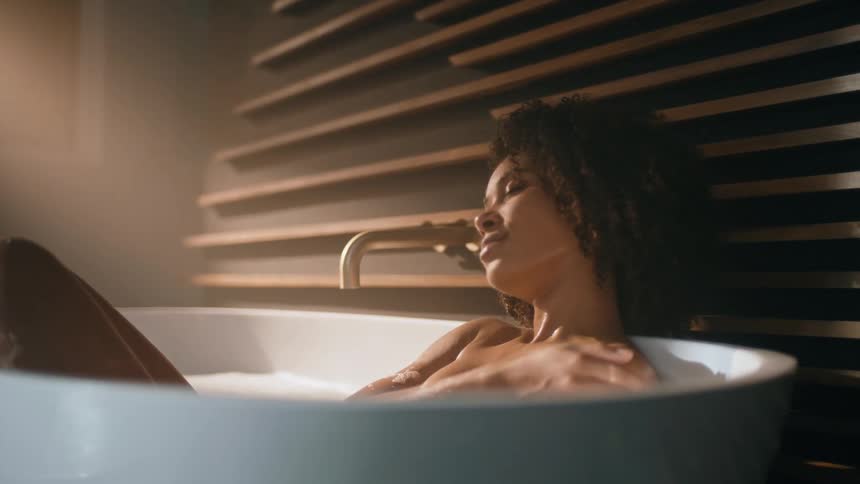 Woman soaks in standalone tub with golden faucet near wooden board decorated wall