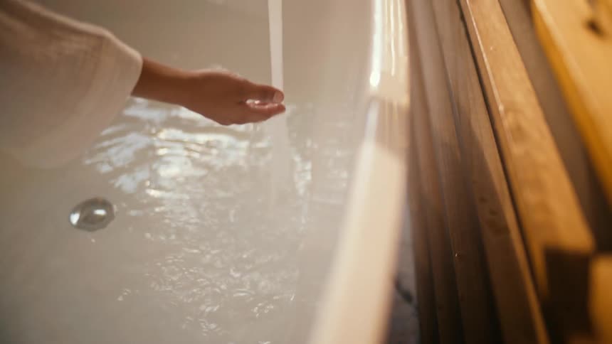 A woman runs her hand through bath water while filling the tub