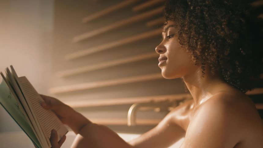 A woman is bathing and reading a book