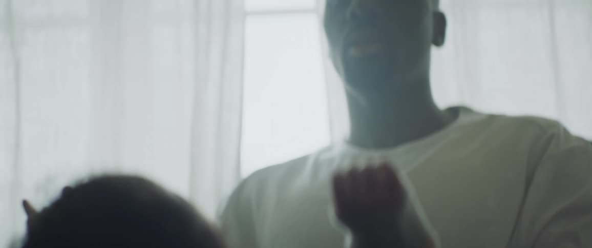 A dad sits in a rocking chair near a window rocking back and forth holding a baby boy in his hands out in front of him