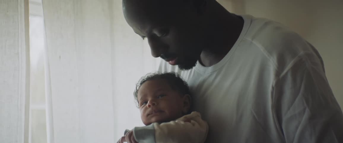 A man in a white shirt holding an infant in his arms swaying back and forth next to a window