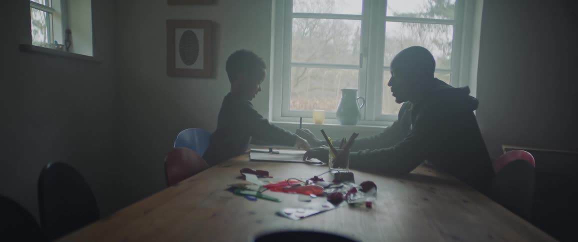 A father and son sit across from each other at a table while the father helps the song draw