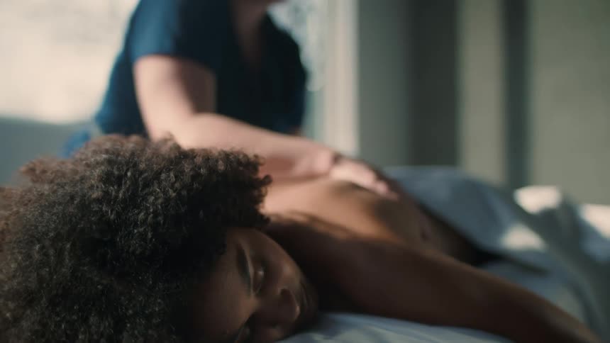 Masseuse massages back of woman lying on her stomach on bed