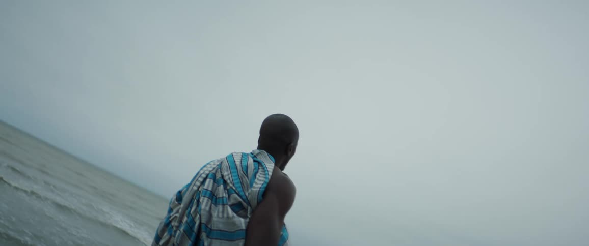 Man with towel stands still looking around on the beach on cloudy day
