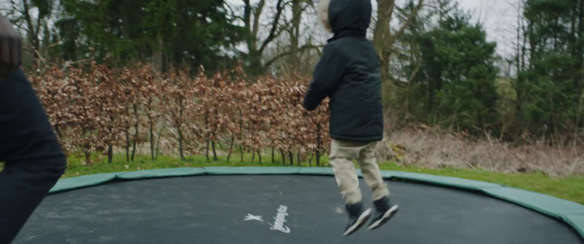 An adult and child getting on a trampoline and jumping outdoors
