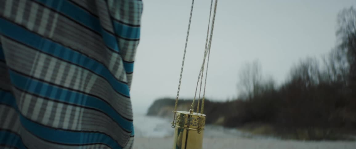 A person is walking along the beach carrying a gold chained pot that has smoke coming from it