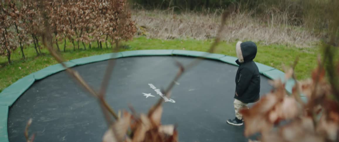 A young boy in a parka bounces on a trampoline in slow motion