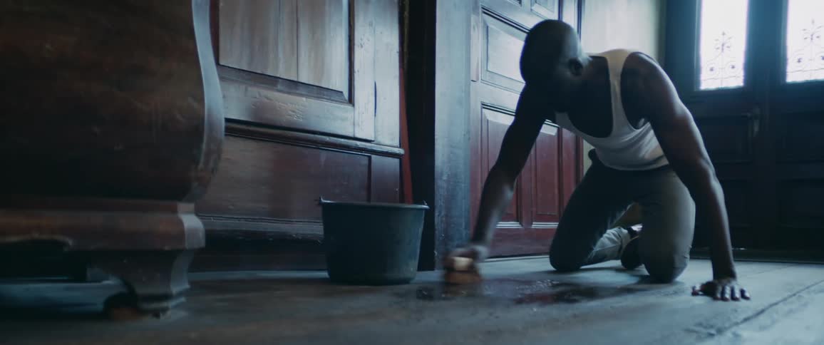 Man kneels scrubbing floor in room with wooden walls with a brush