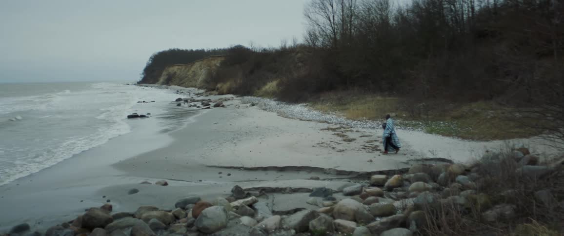 A person is walking down to a coastal shoreline in the early morning that is empty with no one else around as the waves crash and the coastal cliffs stretch out down the shallow rocky beach