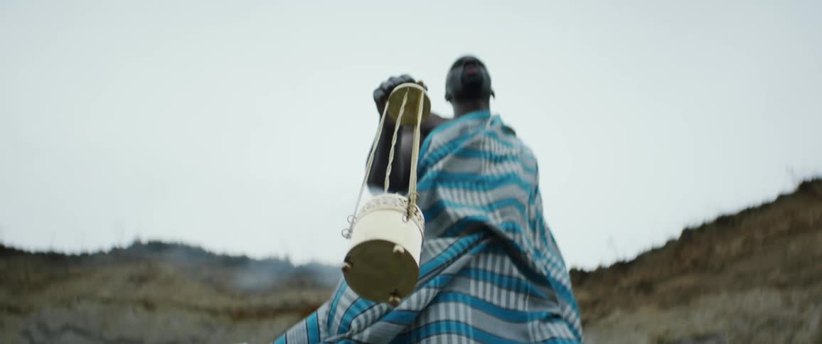 A man wearing a blue checkered cloth swaying a gold cup on a chain with steam rolling out of it