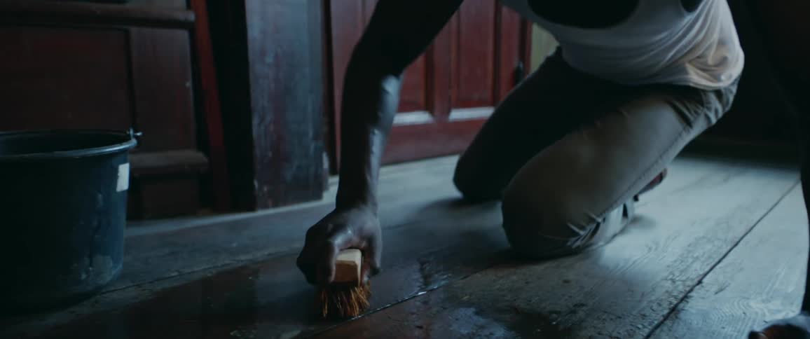 A close up of a man on the floor scrubbing the wood floors with a brush