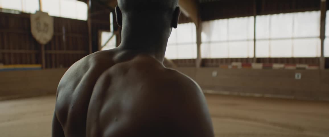 Back of a shirtless strong muscular man walking inside a stable