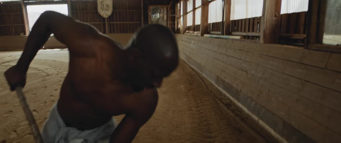 A barechested man shovels dirt inside a big barn show arena