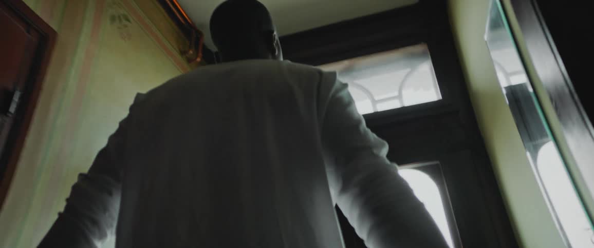 Man wearing long sleeved shirt walks past room toward glass paneled front door