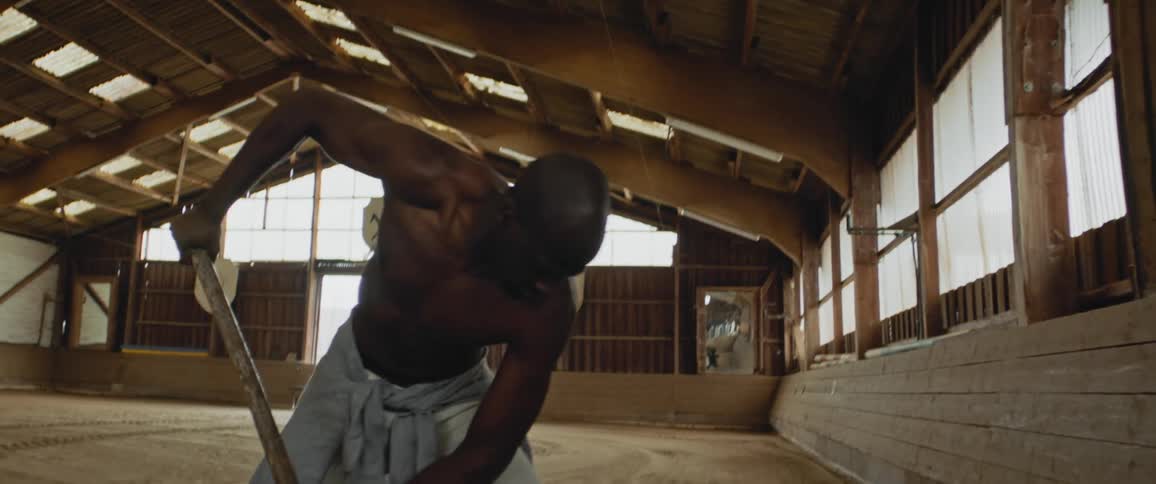 Shirtless worker shovels dirt inside a stable at daytime