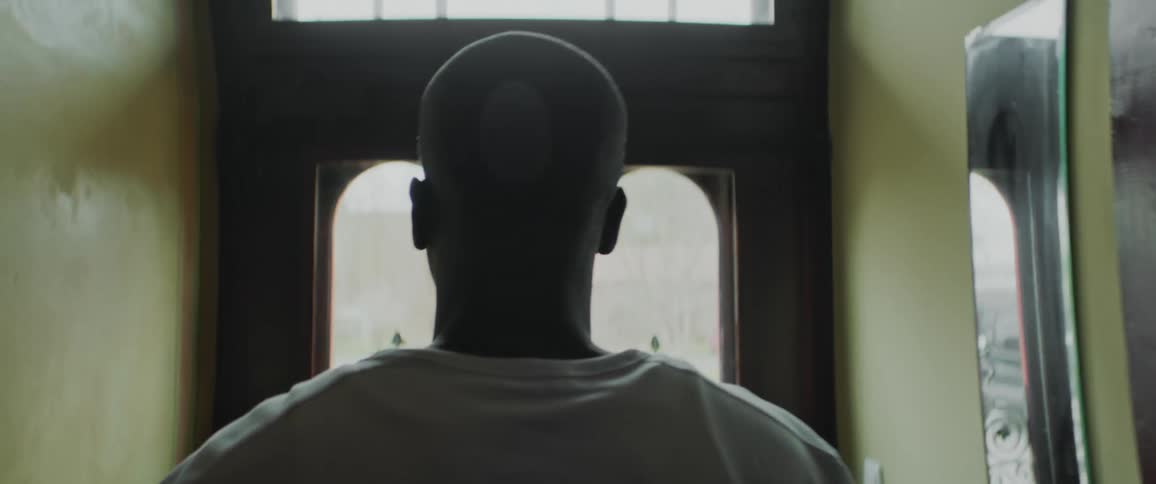Black man walking towards the front door peeking out of the glass