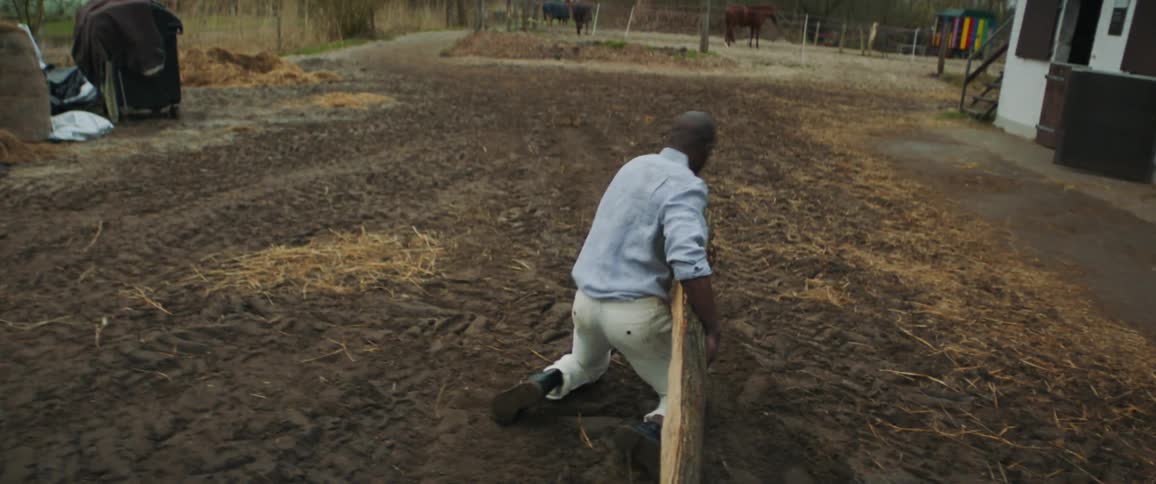 A man is dragging a large log and falls to his knees