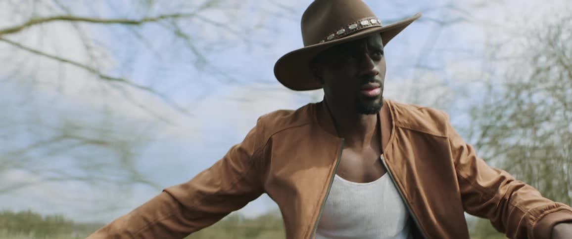 A man wearing a cowboy hat riding on something taking him by trees