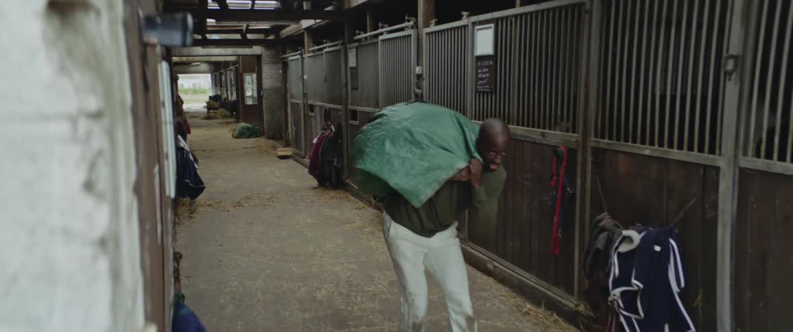 Man working on a stable stumbles under the weight of a bag carried over his shoulders