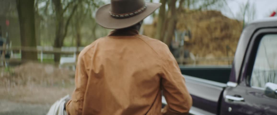 A man walking towards a pickup truck carrying a bag and jumping into the bed of the truck