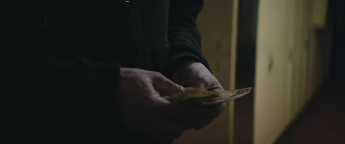 A person is standing in a hallway counting a handfull of money and they pass it to the hands of another person