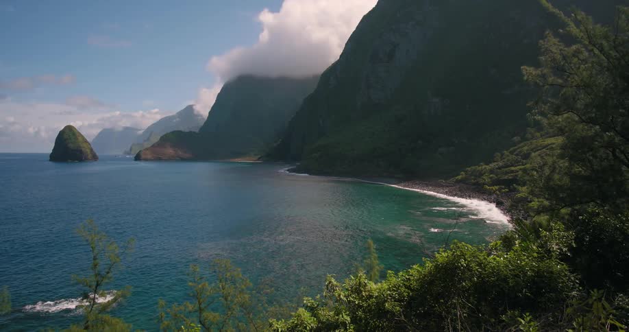 An ocean coastline with waves crashing up against a rocky shore with mountain cliffs at the oceanside