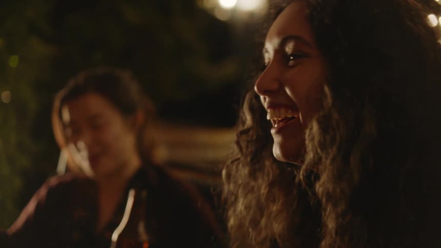 Two women sit next to each other laughing and smiling and talking to others near them