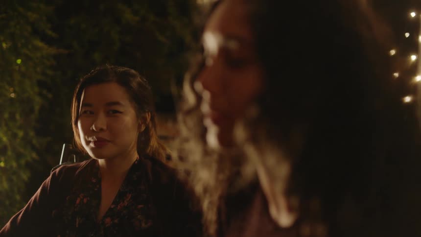 A young woman listens to her female friend talking at an evening gathering