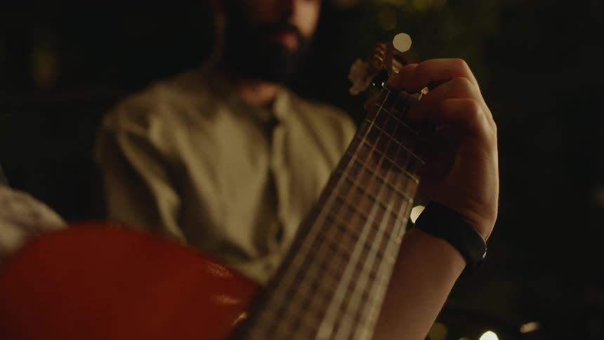 A man moves his hand across the neck of an acoustic guitar as he plays