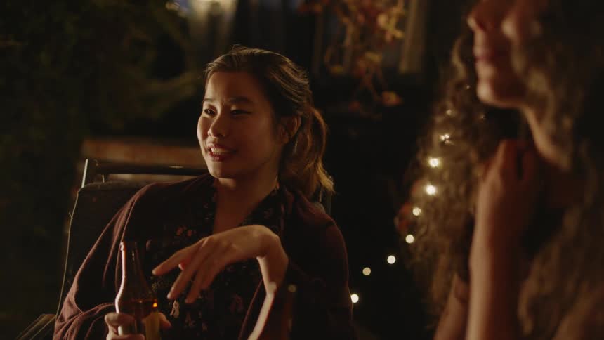 Two women sitting next to each other both with a beer bottle in their hands talking and smiling