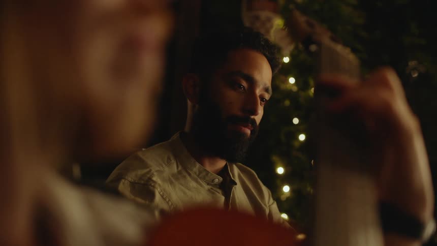 Young bearded man listens to a friend playing acoustic guitar at a party