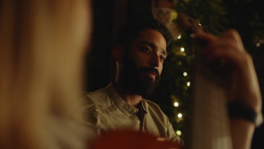 Young bearded man listens to a friend playing acoustic guitar at a party