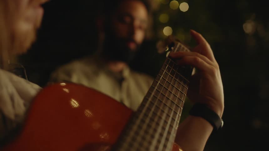 Two people are sitting outdoors and playing the guitar