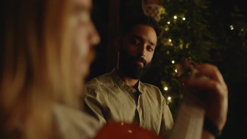 Young bearded man listens to a friend playing acoustic guitar at a party
