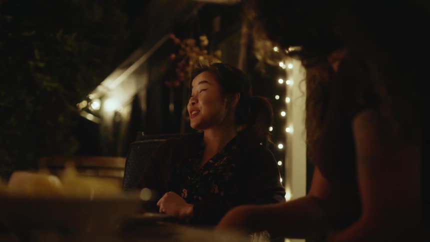 Woman with shirt talks to person laughing sitting at table at night