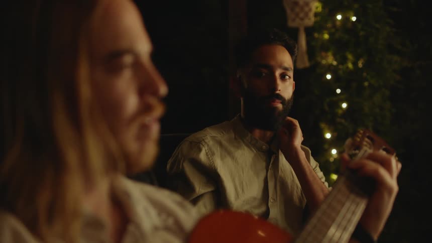 Two men are outdoors and playing the guitar