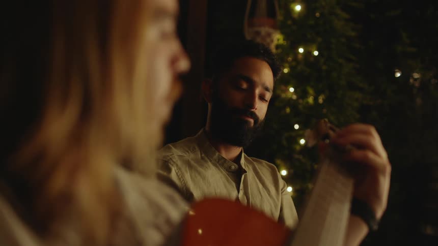 A man sits next to and watches another man playing a string instrument