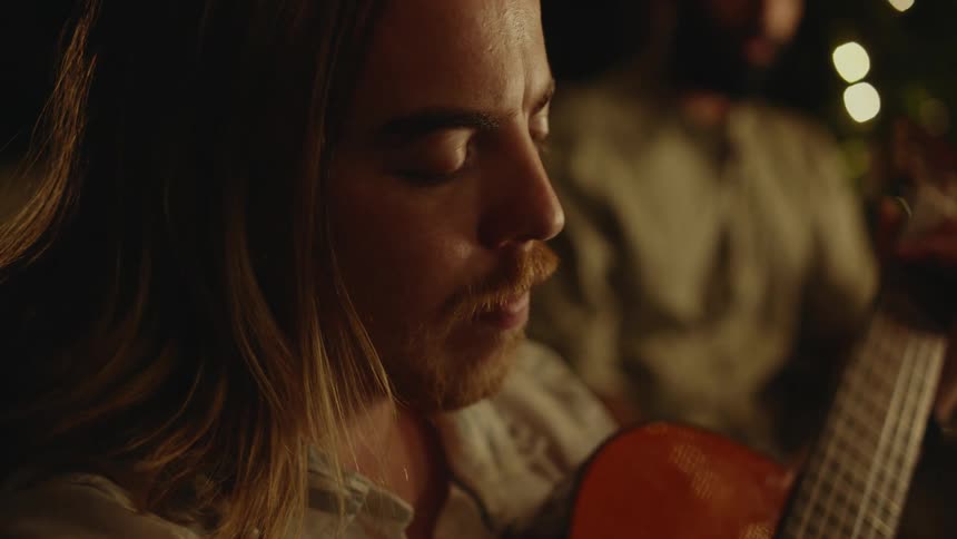 Man plays acoustic guitar for a group of friends at a party