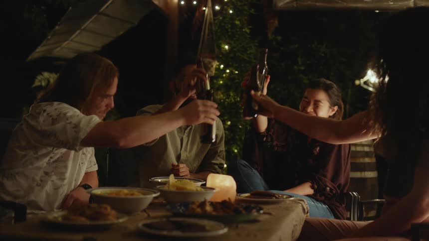 Four young adults have a toast over food and better at an oudoor nighttime gathering