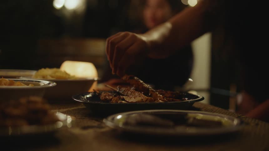 An up close of a table full of food with people sitting around it grabbing the food