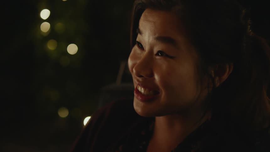 Close up of the face of a young woman laughing and talking to friends in a cozy room
