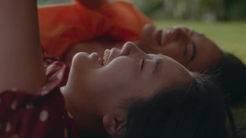 Two women are laying in the grass and laughing together