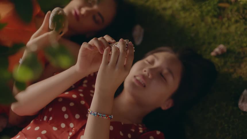 Two women look at crystals while lying on the grass