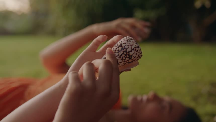 Two people lie on their backs on lawn while examining seashells