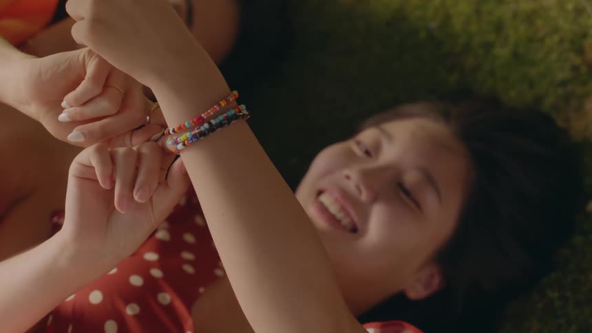 A close up of a womans arm with bracelets on it and her smiling next to another woman laying on the ground