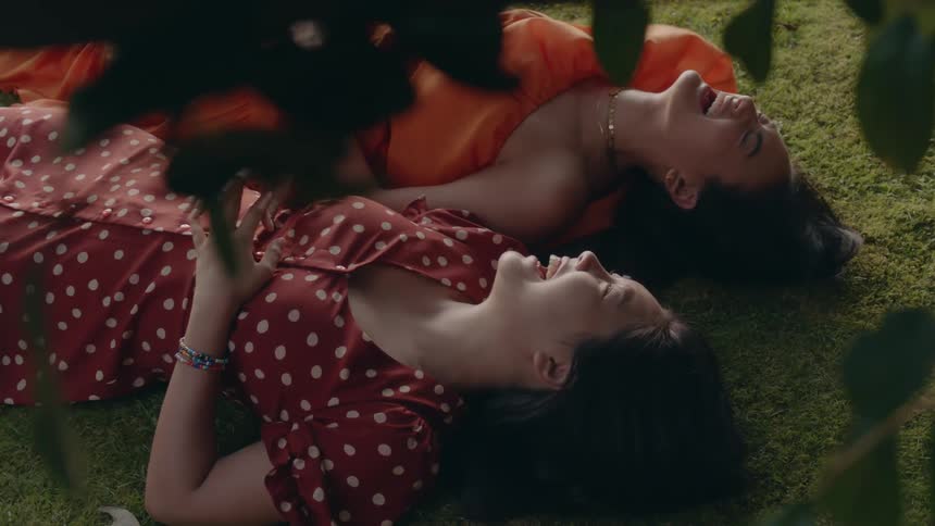 Two women lying on lawn overcome with laughter