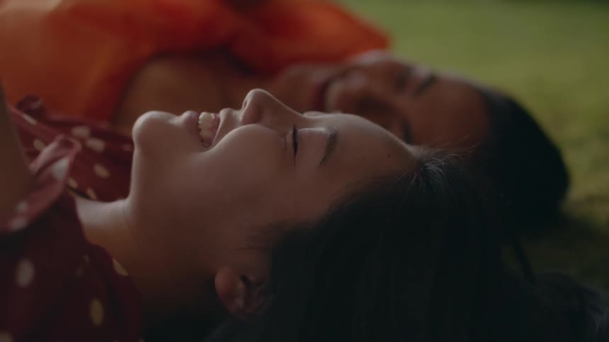 Two women lying on the grass laugh while conversing
